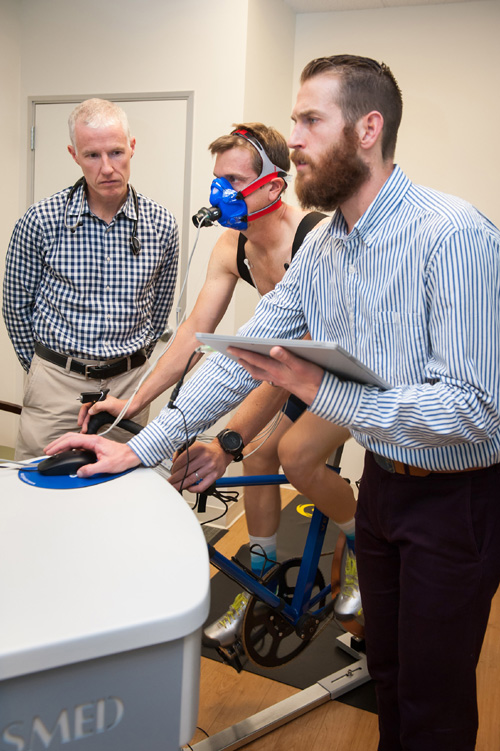 Two male doctors observing man hooked up to breathing equipment while bicycling.